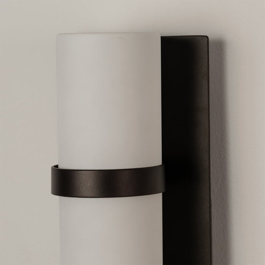 Closeup of black metal wall sconce with frosted cylindrical glass shade highlighting premium indoor lighting design.
