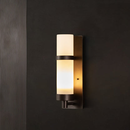 Black metal wall light with illuminated frosted glass shade on dark background creating warm indoor ambient lighting.