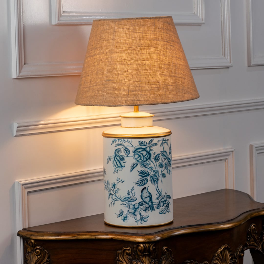 White ceramic floral table lamp with brown fabric shade placed on wooden console for warm ambient home lighting.