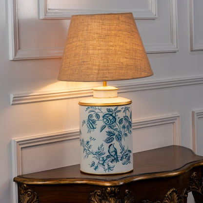 White ceramic floral table lamp with brown fabric shade placed on wooden console for warm ambient home lighting.