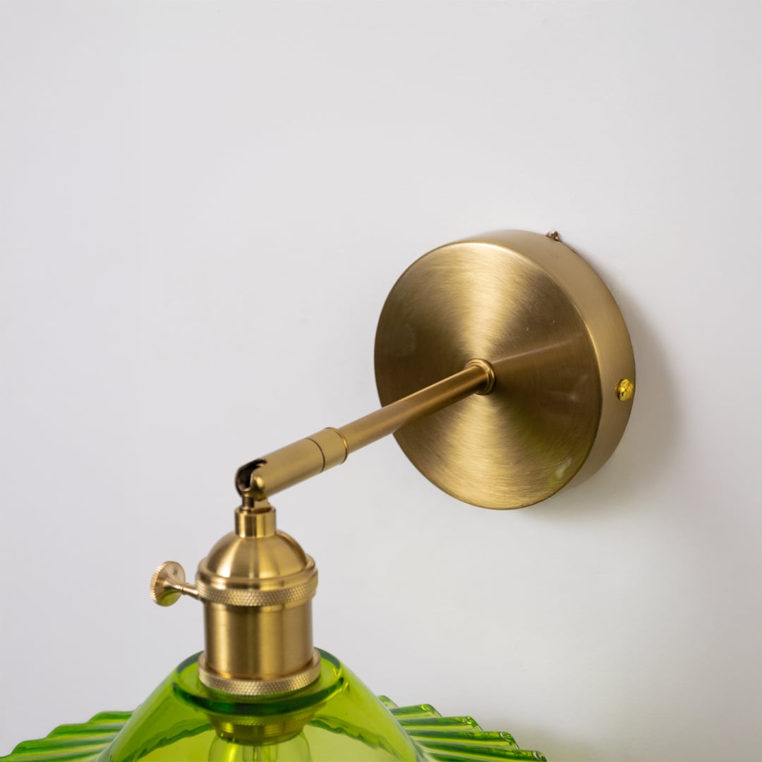 Closeup of gold metal wall light with green glass shade for luxury ambient lighting decor styling ideas.