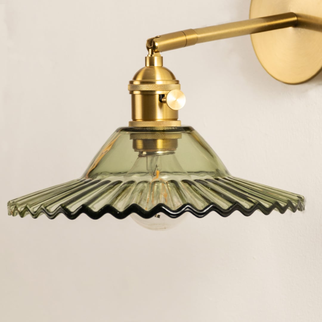 Closeup of gold metal wall light with green ribbed glass shade for elegant lighting decor styling ideas.