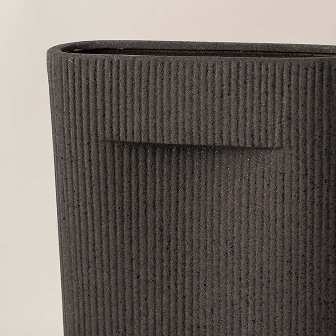 Black ribbed ceramic vase closeup with vertical texture placed on white surface against neutral background highlighting detailed craftsmanship and modern decor appeal.
