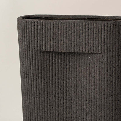 Black ribbed ceramic vase closeup with vertical texture placed on white surface against neutral background highlighting detailed craftsmanship and modern decor appeal.