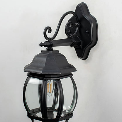 Closeup view of outdoor wall lantern showing detailed black metal arm mounting plate and clear glass panels with visible bulb holder and textured finish.
