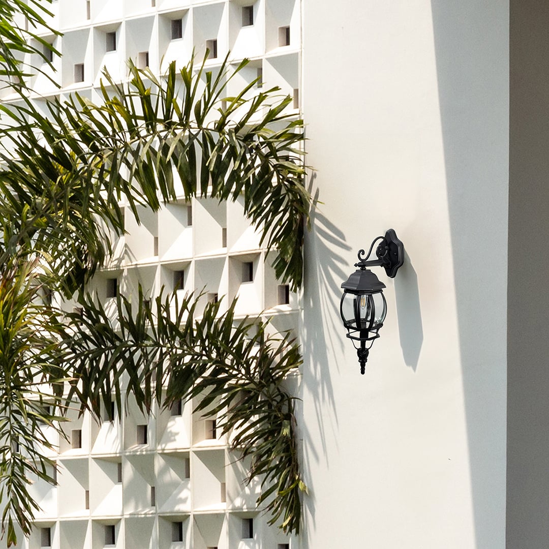 Black upward outdoor wall lantern with curved glass scroll bracket illuminating entrance creating vintage coach exterior light.