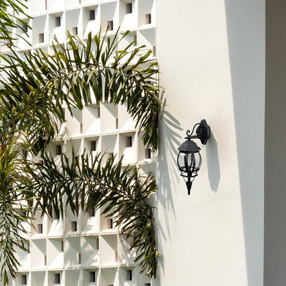 Black upward outdoor wall lantern with curved glass scroll bracket illuminating entrance creating vintage coach exterior light.