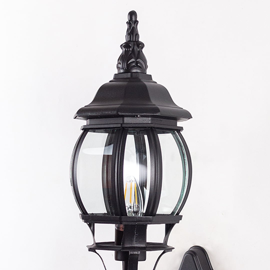 Closeup of black upward wall lantern showing curved glass cage scroll bracket detail and decorative finial vintage design.