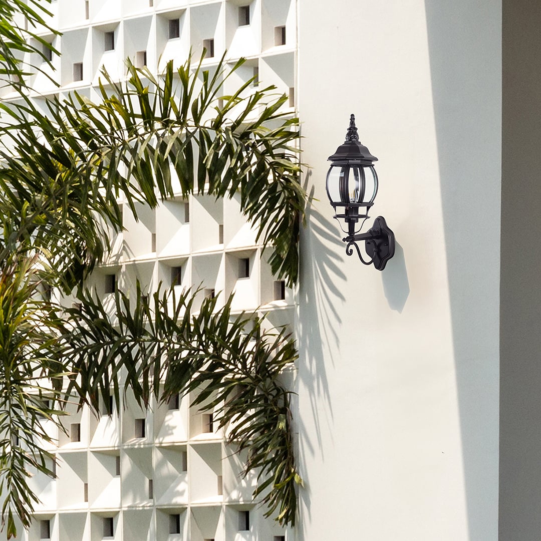 Black upward outdoor wall lantern with ornate scroll bracket illuminating entrance creating elegant vintage coach lighting style.
