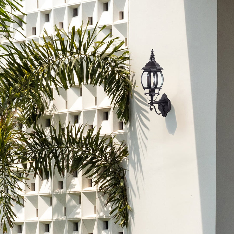 Black upward outdoor wall lantern with ornate scroll bracket illuminating entrance creating elegant vintage coach lighting style.