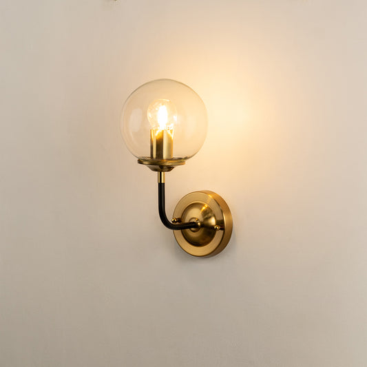 Wall light with clear glass globe and gold metal mount emitting warm glow ideal for modern bedroom or hallway wall decor placement.
