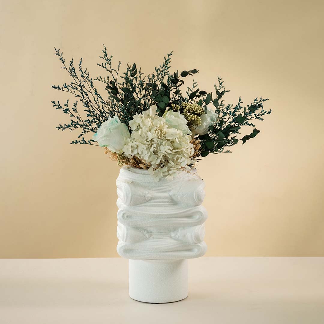 White sculptural ceramic vase with modern textured design styled on a wooden coffee table against white background.