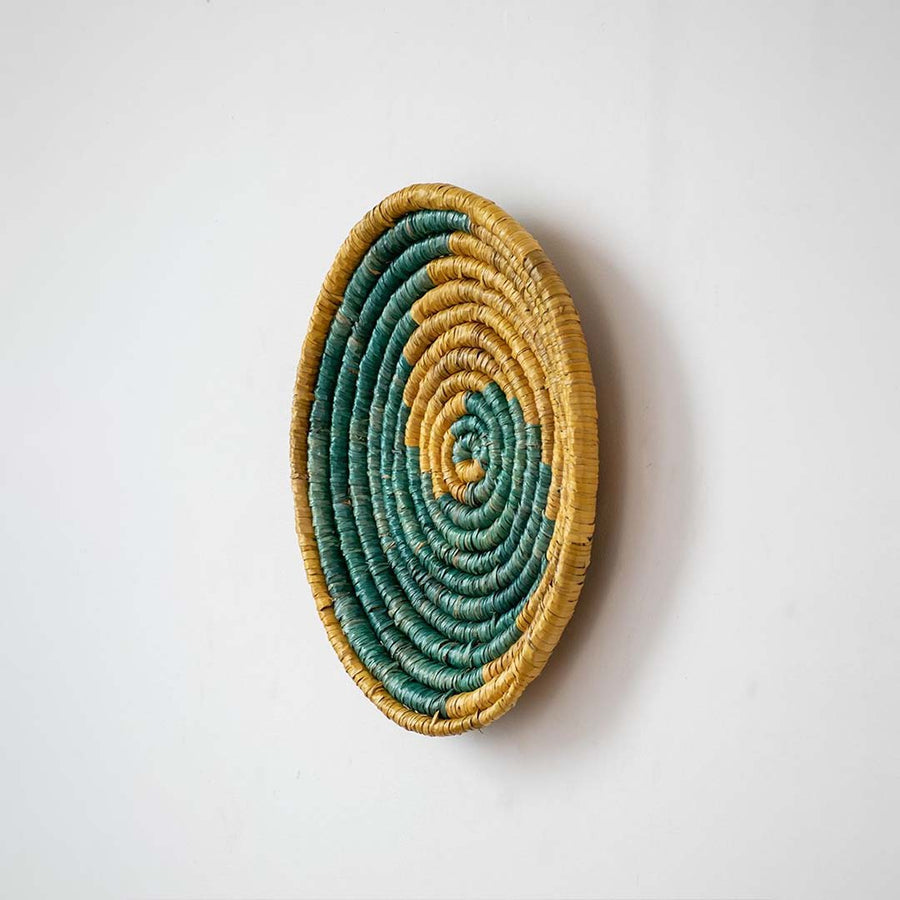 Side view of round woven wall basket with layered natural and teal fibers highlighting thickness depth and handcrafted detailing.