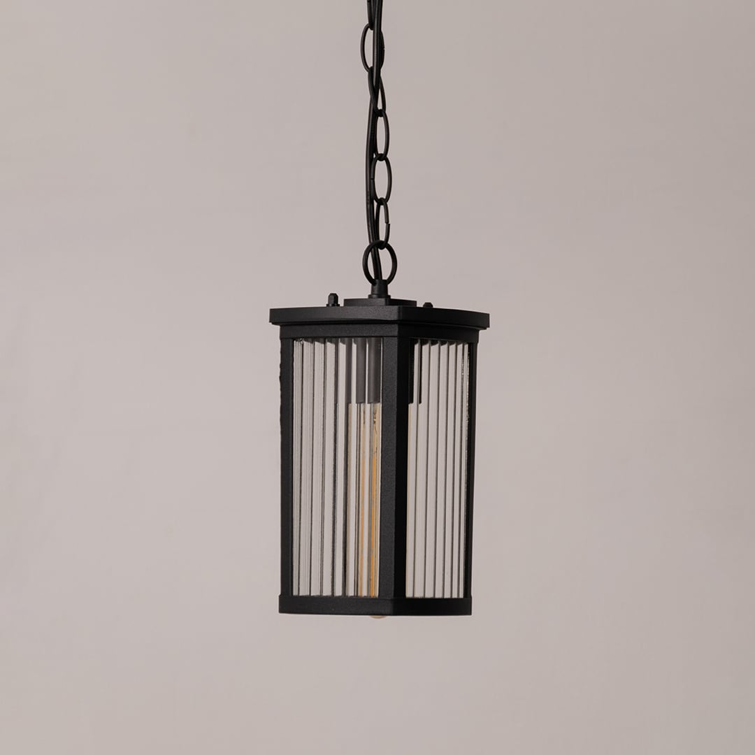 Black metal lantern with ribbed glass shown on white background displaying sleek outdoor lighting design.