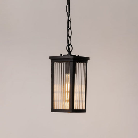 Black metal hanging lantern lit on white background highlighting warm glow and ribbed glass for home lighting.