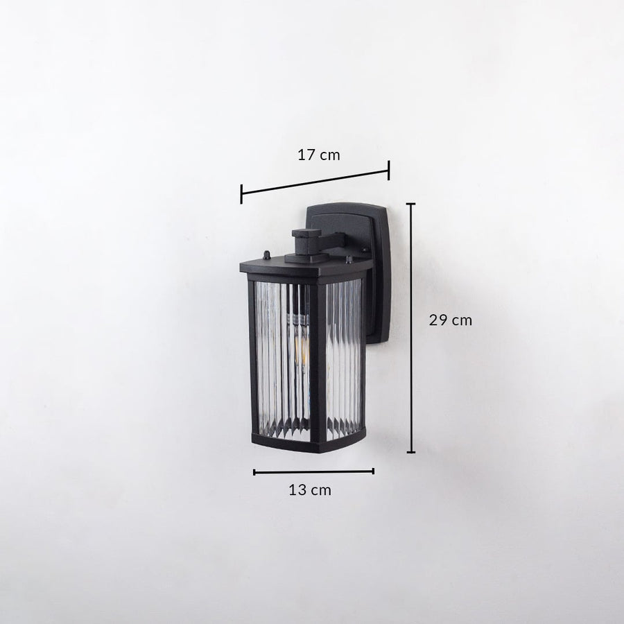 Outdoor wall light with ribbed glass and black frame shown on white background with 29 cm height 17 cm width 13 cm depth.