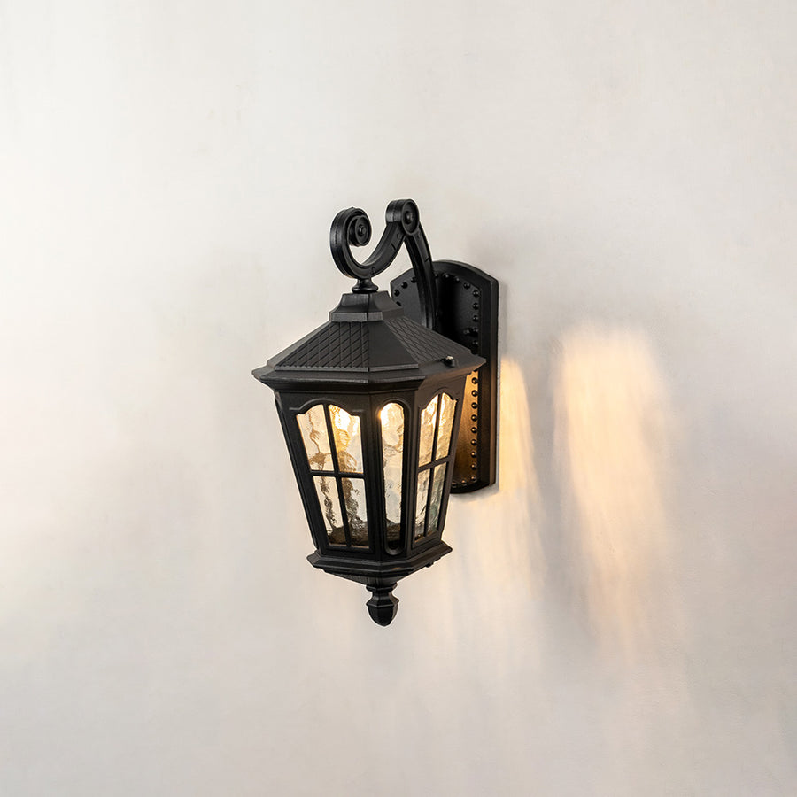 Black metal outdoor wall light on white background with paneled glass shade casting a warm sidelight for villa decor.