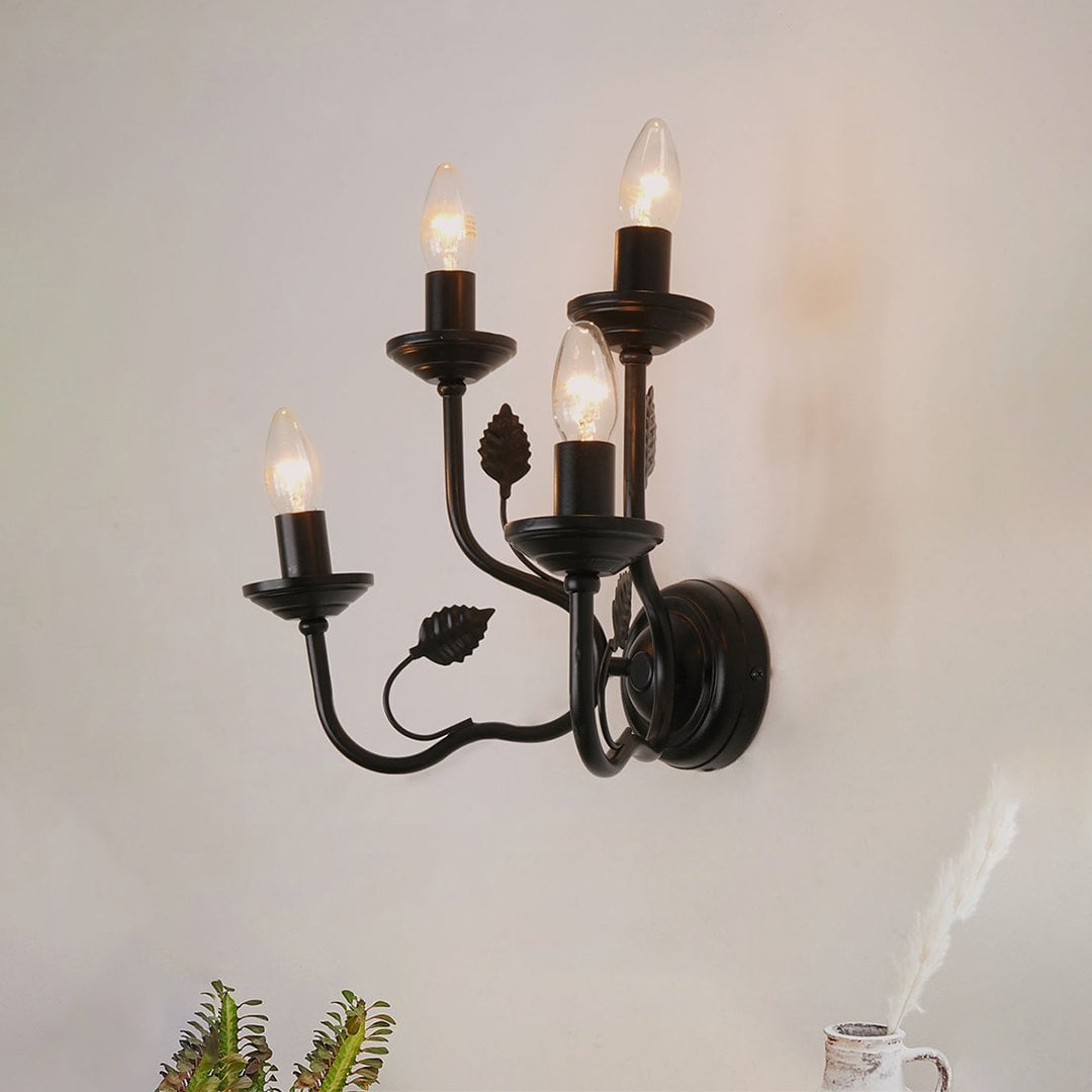 A black wall sconce with four bulbs turned off set against a white background showing its elegant curved metal arms and leaf inspired accents.