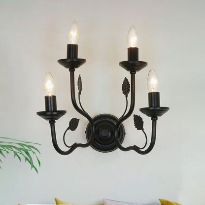 A classic black four light wall sconce glowing warmly in a soft neutral living space adding elegant lighting with curved metal arms and leaf accents.