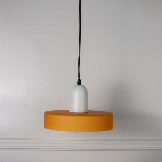Minimal pendant light with white and yellow shade and hanging cord placed against neutral wall background highlighting clean modern lighting decor aesthetic.