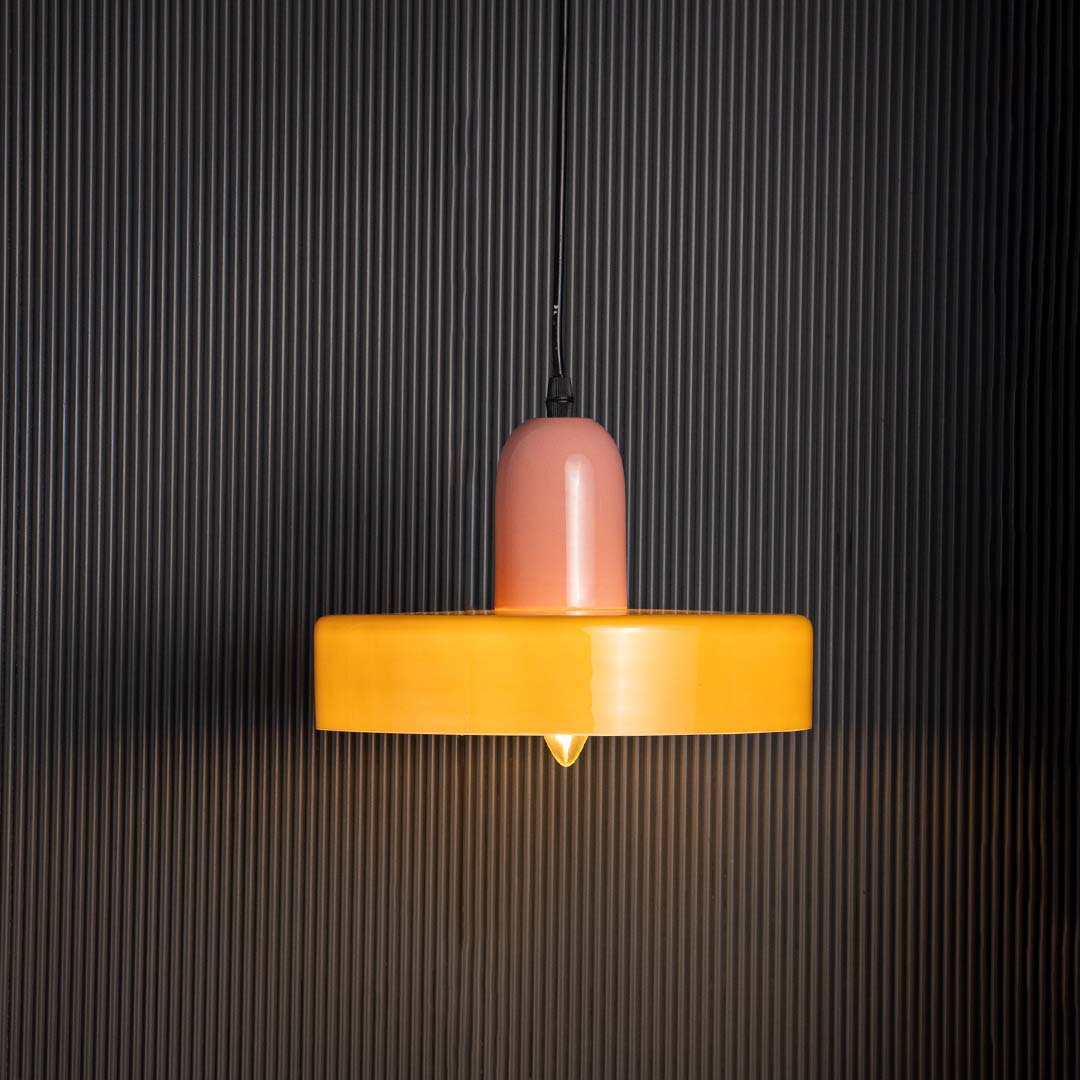 Pink and olive green pendant ceiling light glowing beautifully with warm light against black background creating luxury decor.