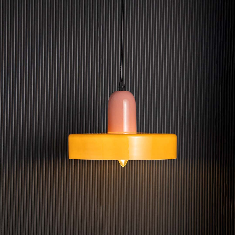 Pink and olive green pendant ceiling light glowing beautifully with warm light against black background creating luxury decor.