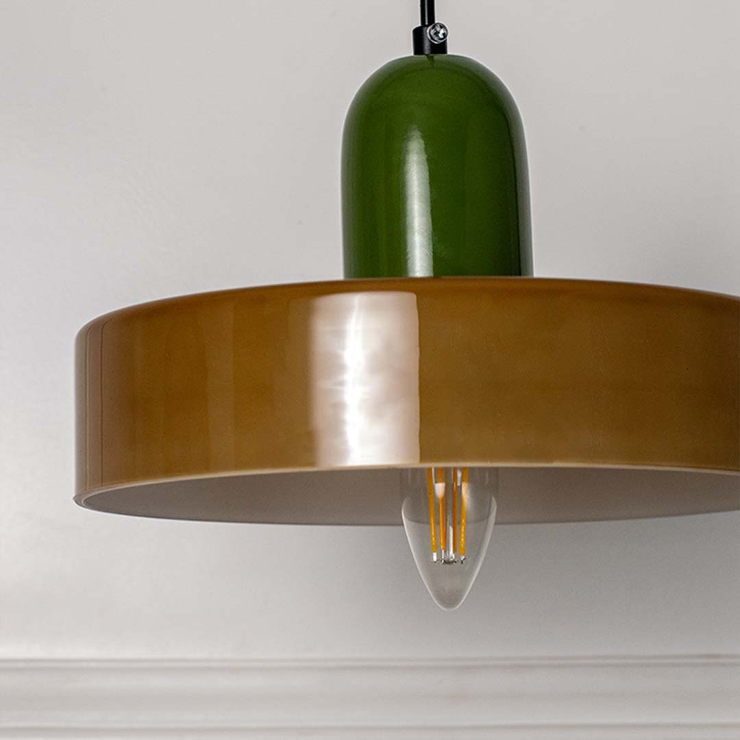 Green and wood pendant light with flat circular shade and hanging cord placed against neutral wall background showcasing mid century modern lighting styling.