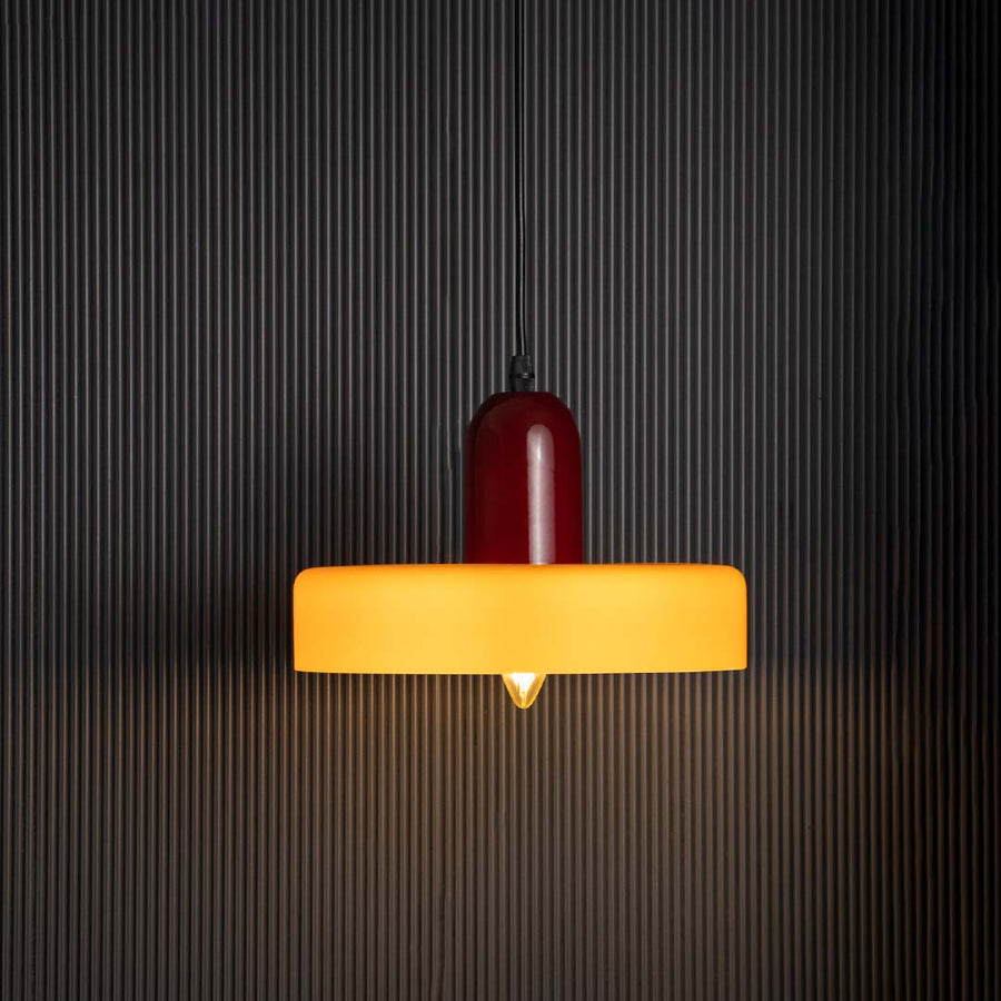 Mustard yellow and red pendant ceiling light glowing beautifully against dark black background creating modern decorative style.