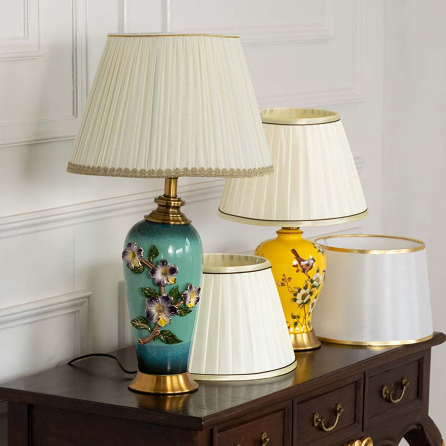 Pleated shade floral ceramic table lamp on wooden sideboard with light on for vintage decorative home décor.