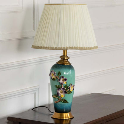 Pleated shade floral ceramic table lamp on wooden side table with light on for vintage decorative home décor.