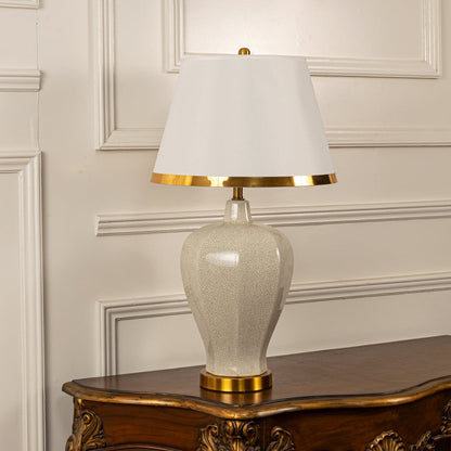 White shade beige ceramic table lamp on carved console table with light off and white panel wall background for classic elegant décor.