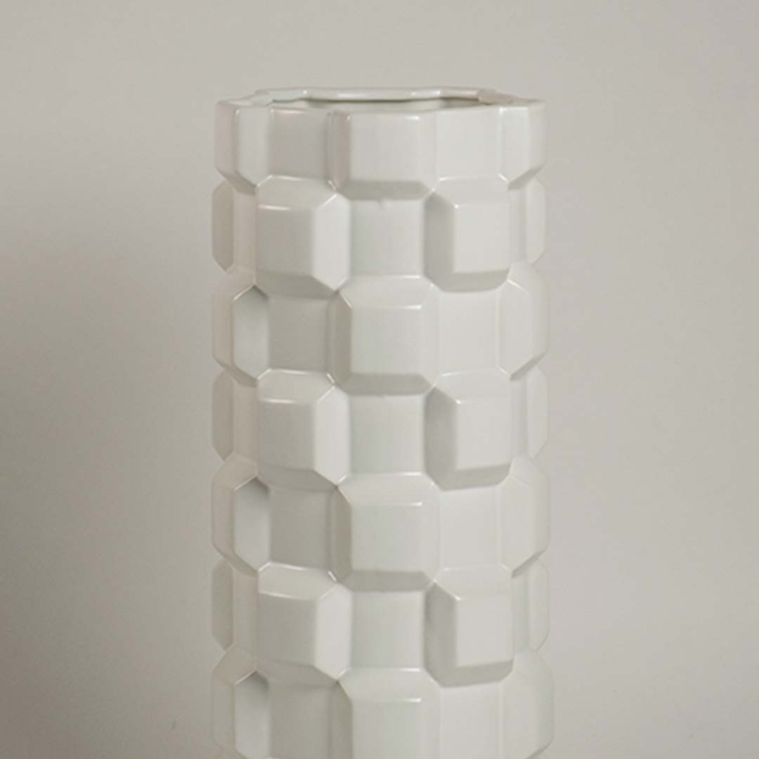 Closeup image of a white ceramic cylinder vase featuring a bold three-dimensional geometric blocky puzzle relief texture.