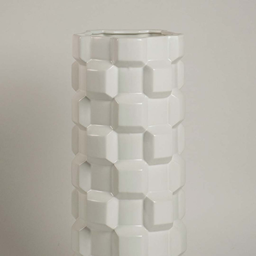 Closeup image of a white ceramic cylinder vase featuring a bold three-dimensional geometric blocky puzzle relief texture.