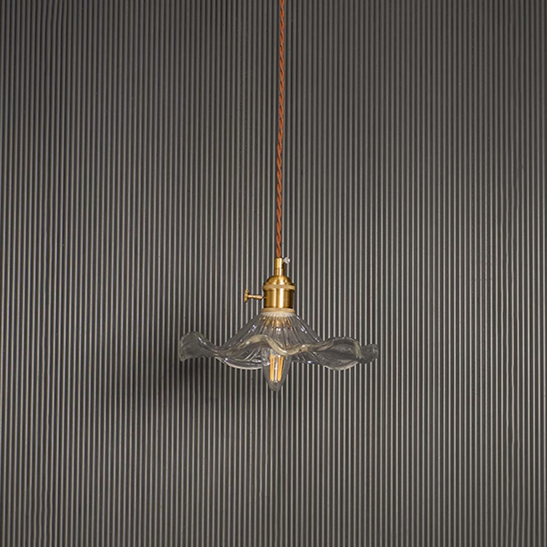 Unlit wavy glass pendant light with brass top and brown cord displayed on white background for minimal aesthetic decor.