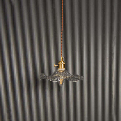 Unlit wavy glass pendant light with brass top and brown cord displayed on white background for minimal aesthetic decor.