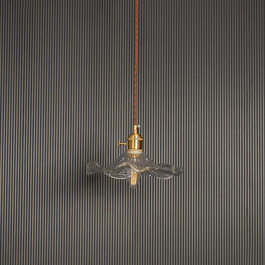 Unlit wavy glass pendant light with brass top and brown cord displayed on white background for minimal aesthetic decor.