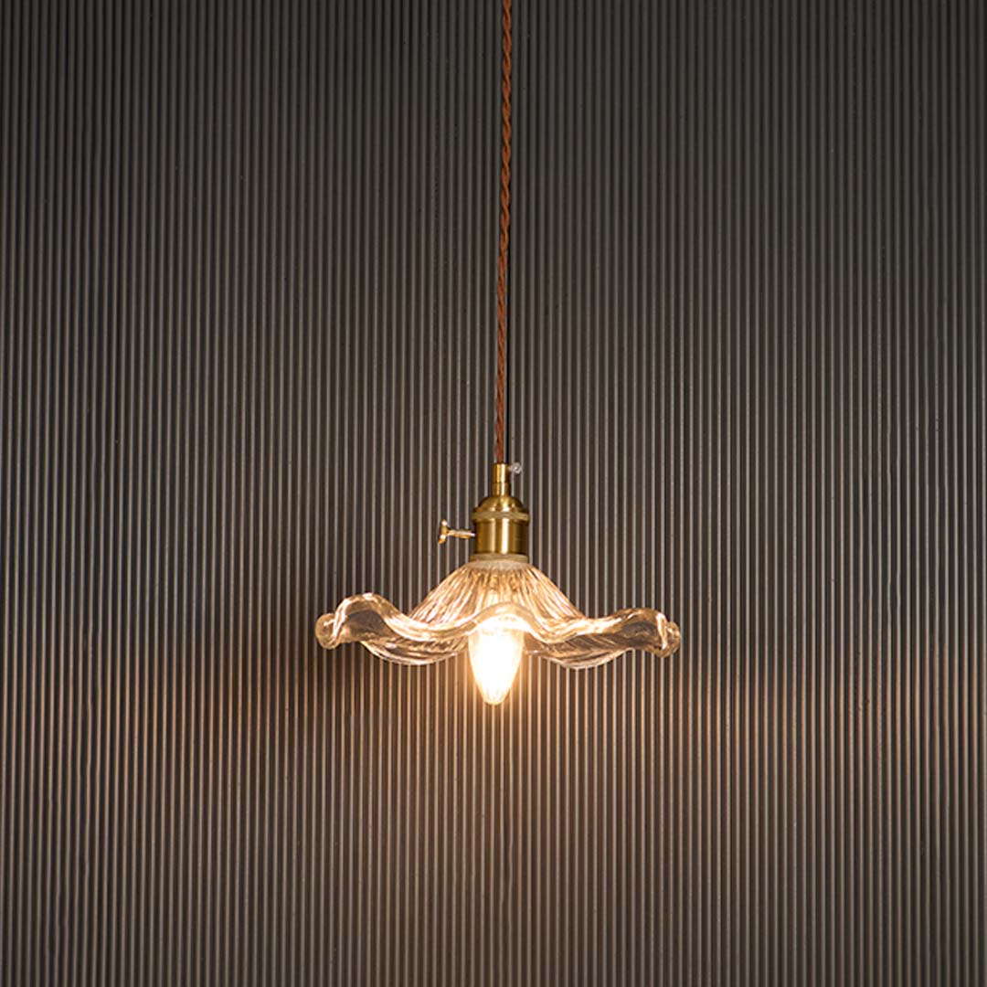 Wavy clear glass pendant light glowing softly with brass holder against black background for sophisticated ambience.