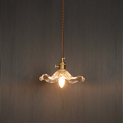 Wavy clear glass pendant light glowing softly with brass holder against black background for sophisticated ambience.