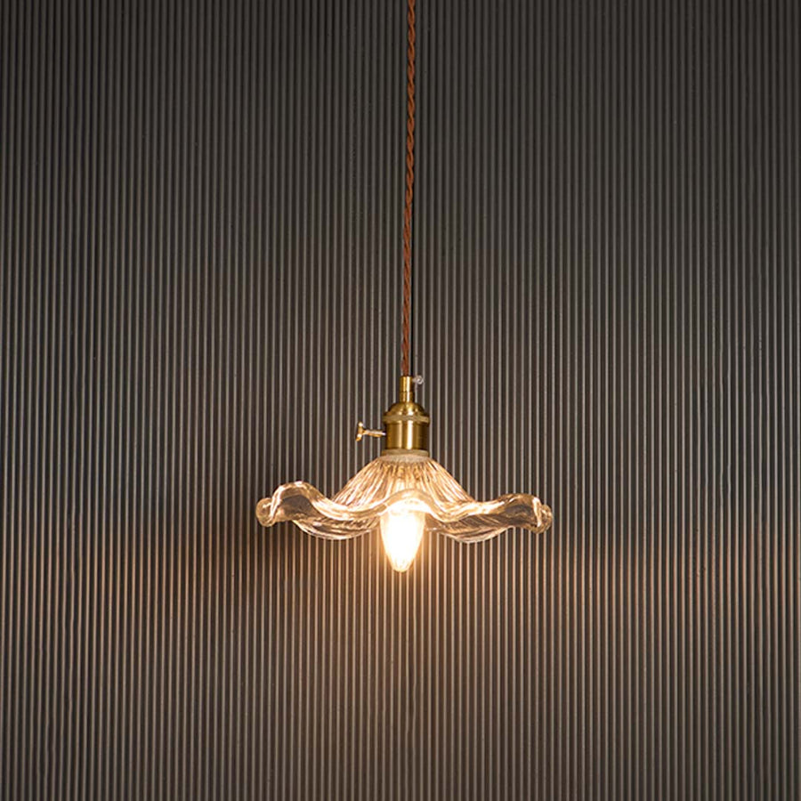 Wavy clear glass pendant light glowing softly with brass holder against black background for sophisticated ambience.