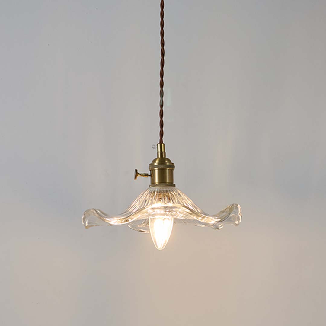 Clear wavy glass pendant light with brass holder glowing warmly on white background for decorative home lighting.