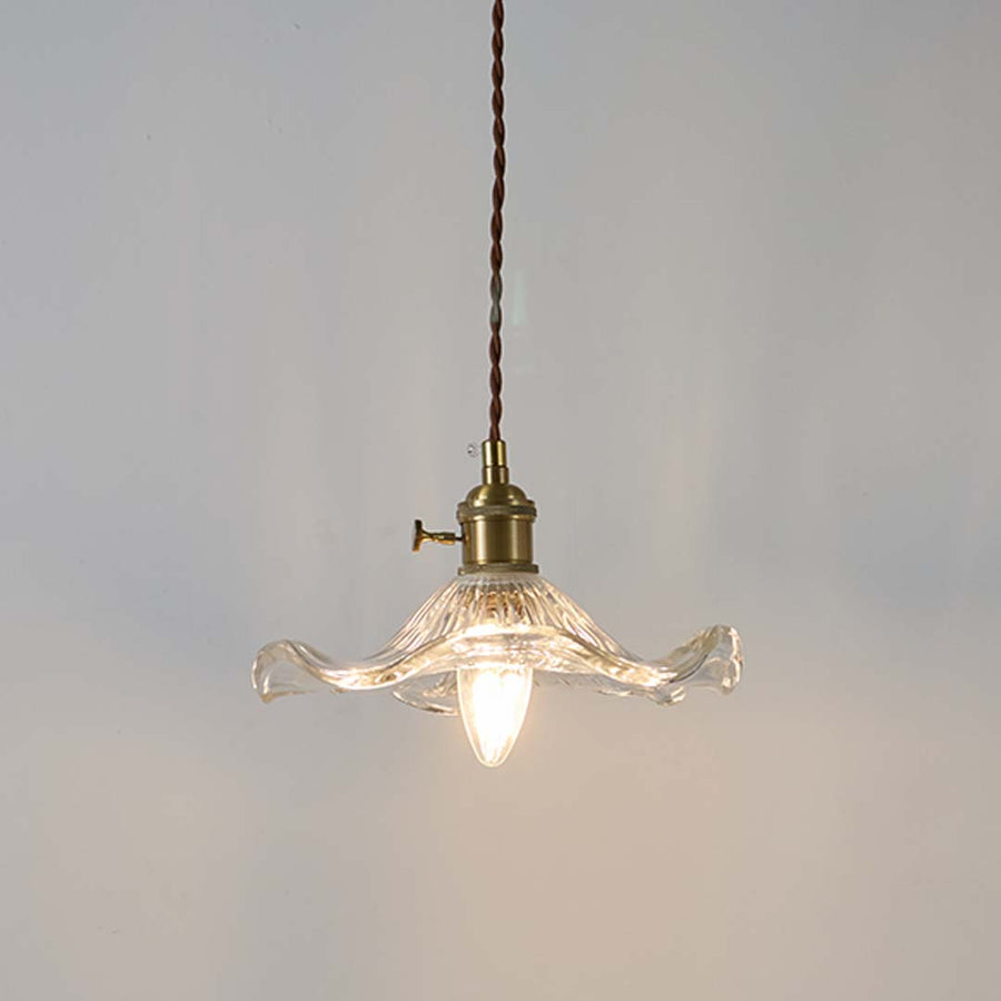 Clear wavy glass pendant light with brass holder glowing warmly on white background for decorative home lighting.