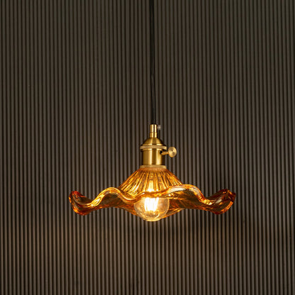 Amber wavy glass pendant light with polished metal holder casting warm ambient glow imagined against a dark background creating a dramatic elegant interior decor mood.