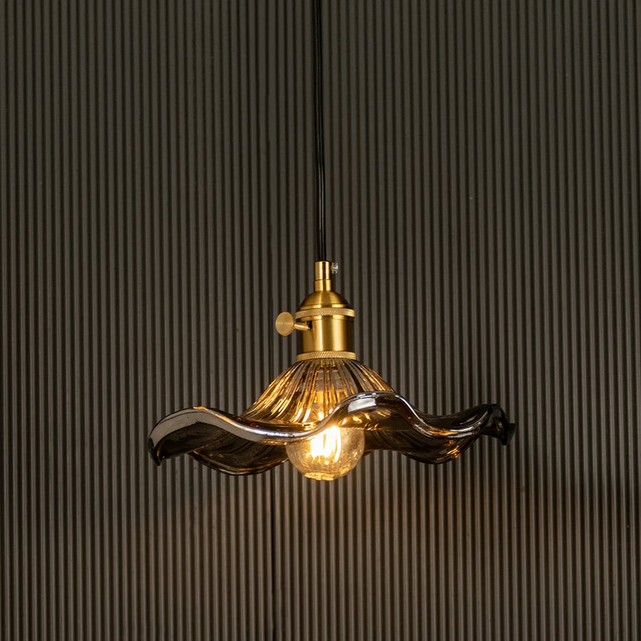 Wavy smoked glass pendant light with a polished metal holder casting soft ambient glow imagined against a dark background creating a dramatic refined interior decor mood.