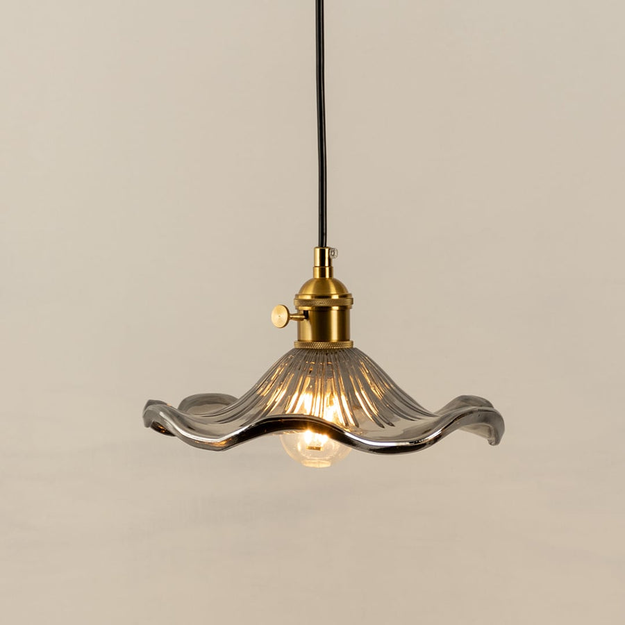 Clear textured glass pendant light with gold metal fixture illuminated to display elegant decorative ceiling lighting.