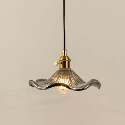 Clear textured glass pendant light with gold metal fixture illuminated to display elegant decorative ceiling lighting.