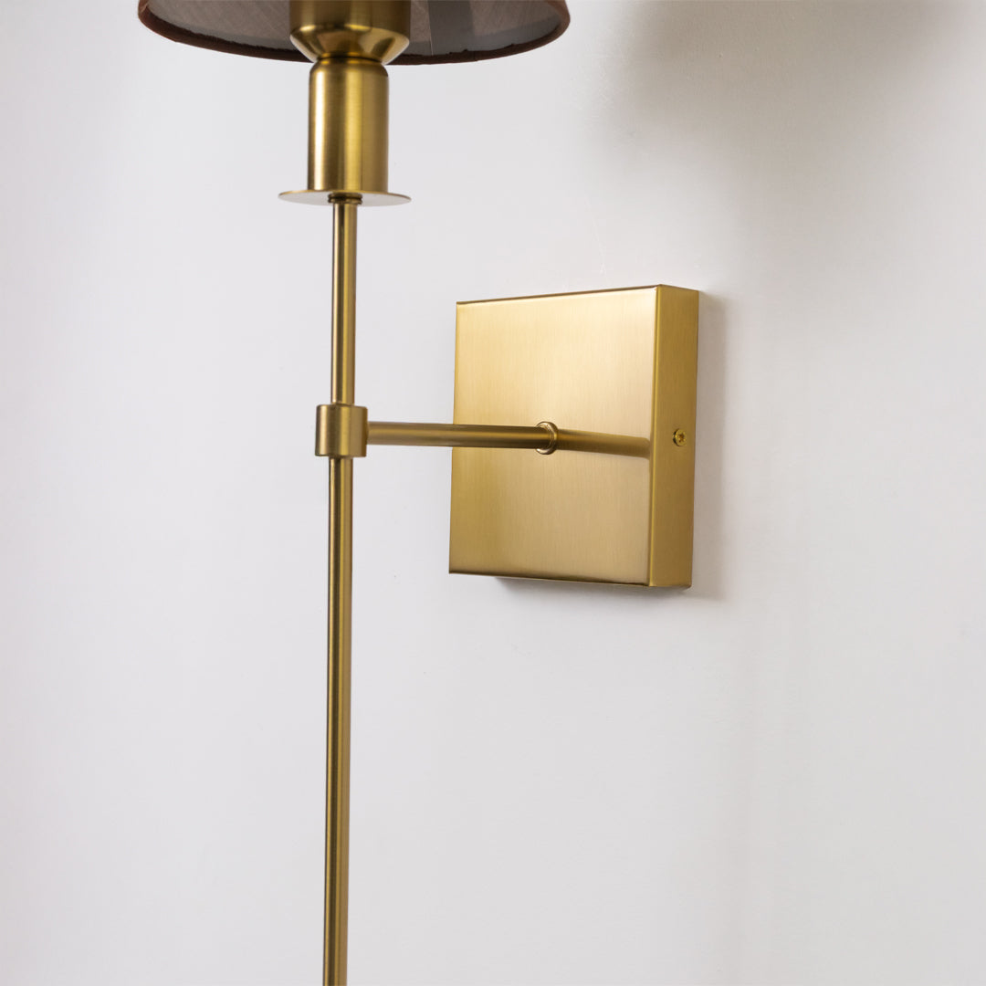 Closeup wall light in gold metal finish with fabric shade and square base for bedroom or living decor lighting white background.