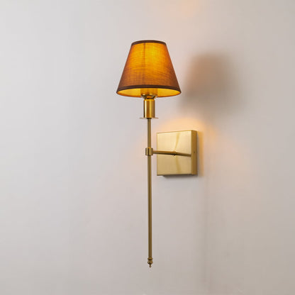 Gold metal wall sconce with brown fabric shade glowing softly on white background for elegant modern home lighting decor.