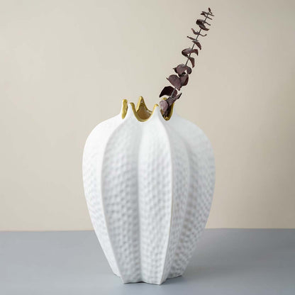 White ceramic vase with gold rim textured finish styled with dried branch for modern home decoration.