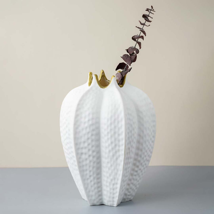 White ceramic vase with gold rim textured finish styled with dried branch for modern home decoration.