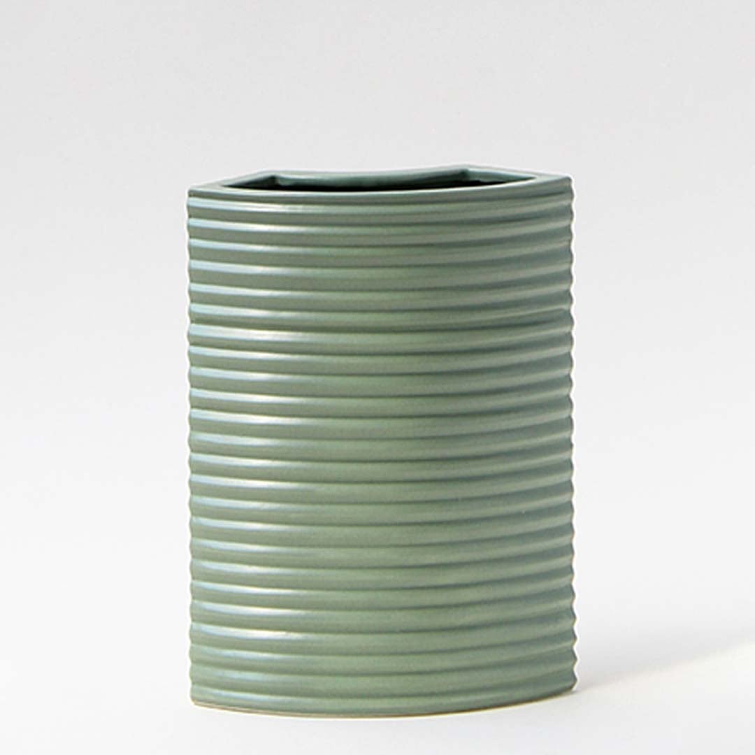 Closeup of green ceramic vase showcasing ribbed lines and smooth matte finish with arrangement in natural light.